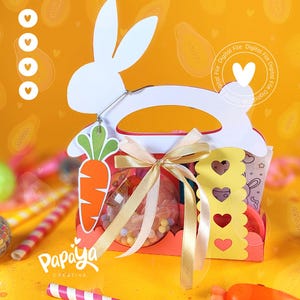 May include: A white bunny-shaped Easter basket with a red and yellow handle. The basket is filled with colorful candies and a clear plastic ball filled with confetti. The basket is decorated with a yellow ribbon and a green carrot.