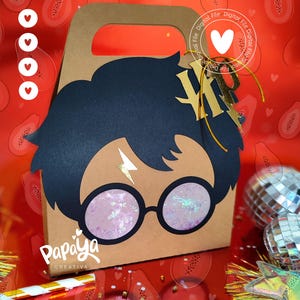 Puede incluir: Una bolsa de regalo de papel marrón con un recorte de la cara de un personaje, con cabello negro, gafas redondas y una cicatriz de rayo. La bolsa tiene un asa y el texto "Papaya Creativa".
