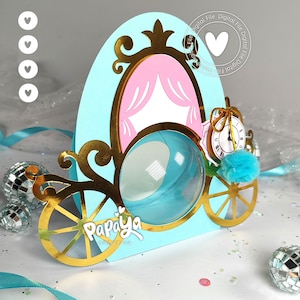 May include: A light blue carriage-shaped box with a gold metallic frame, pink curtain accents, and a clear circular window. The box features a small clock illustration, a turquoise pom-pom, and the white text Papaya Creativa on the front.