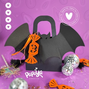Puede incluir: Una bolsa de regalo negra con temática de Halloween con forma de murciélago, con detalles de caramelos naranjas. La bolsa tiene un asa y alas de murciélago. El fondo es morado con formas de papaya y bolas de discoteca.