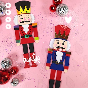 May include: Two colorful paper nutcracker figures with crowns, mustaches, and white hair, set against a pink background with disco balls and red ornaments. One nutcracker is red and black, the other is blue and red. The text "Papaya Creativa" is visible.
