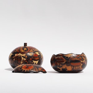 May include: Three handcrafted, decorative gourd vessels with intricate, carved designs. The set includes a round lidded container, a shallow bowl, and a lid. The gourds feature warm brown and orange tones, with detailed depictions of figures and patterns.