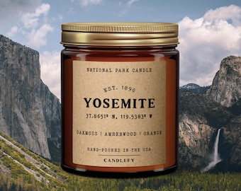 May include: A brown glass candle jar with a gold lid. The label reads "National Park Candle", "Est. 1890", "Yosemite", "37.8651° N, 119.5383° W", "Oakmoss | Amberwood | Orange", "Hand-poured in the USA", and "Candlefy".
