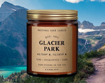 May include: A brown glass candle jar with a gold lid. The label reads "National Park Candle", "Est. 1910", "Glacier Park", "48.7596° N, 113.7870° W", "Pine | Eucalyptus | Sage", "Hand-poured in the USA", and "Candlefy".