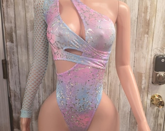 May include: A one-shoulder bodysuit in a pastel color scheme of pink, blue, and purple. The fabric has a shimmering, textured pattern. One arm is covered with a light blue fishnet sleeve. The bodysuit has cut-out details at the waist and neckline.