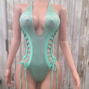 May include: A light green swimsuit with a plunging neckline and lace-up detailing on the sides.