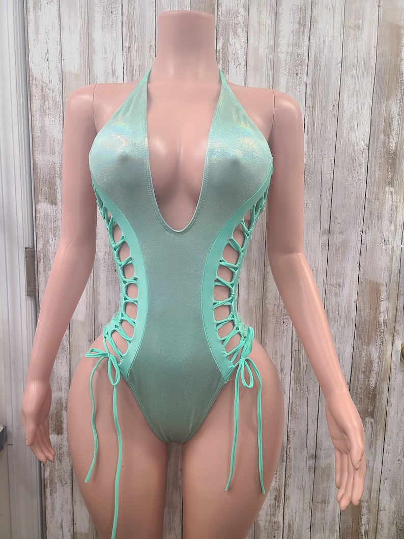 May include: A light green swimsuit with a plunging neckline and lace-up detailing on the sides.