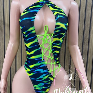 May include: A black, green, and blue swimsuit with a neon green lace-up detail in the front. The swimsuit has a halter neck style and a high-cut leg.