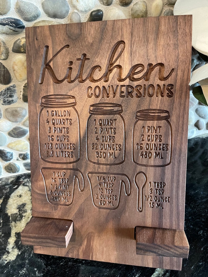 May include: A wooden kitchen conversion chart with engraved measurements for gallons, quarts, pints, cups, ounces, and milliliters. The chart is labeled "Kitchen Conversions".