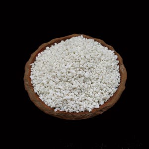 May include: A terracotta bowl filled with small, white, irregularly shaped pebbles. The pebbles are tightly packed, creating a textured surface. The bowl sits against a solid black background.