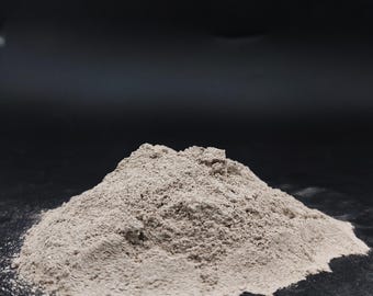 May include: A small pile of light brown powder against a dark background. The powder has a fine, granular texture and appears to be a dry substance. The image is a close-up shot, highlighting the texture and color of the powder.