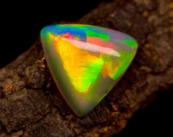 May include: A vibrant, triangular opal gemstone with a mesmerizing play of color. The gem displays a spectrum of hues, including green, yellow, blue, and red, set against a dark, textured background. The opal's surface reflects light, creating a dazzling effect.