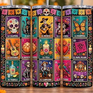 May include: A cylindrical metal tumbler with a straw featuring a colorful grid pattern of fifteen Day of the Dead themed illustrations, including a skull, cat, musician, butterfly, guitar, candle, heart, and altar, all labeled with Spanish text.