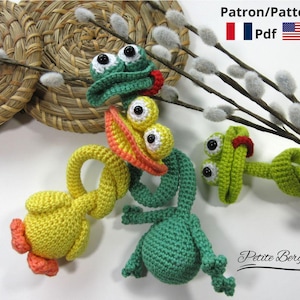 Puede incluir: Juguetes de ganchillo de rana y pato en verde, amarillo y naranja. Los juguetes tienen ojos grandes y saltones y están dispuestos con ramas de sauce y una cesta tejida. La imagen incluye el texto "Patron/Pattern Pdf" y el logotipo de Petite Bergère.