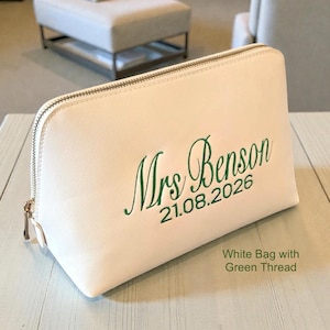 Może przedstawiać: Biała kosmetyczka z zapięciem na zamek błyskawiczny. Torba jest haftowana słowami "Mrs. Benson" i datą "21.08.2026" zieloną nicią. Widoczny jest r&oacute;wnież tekst "White Bag with Green Thread".