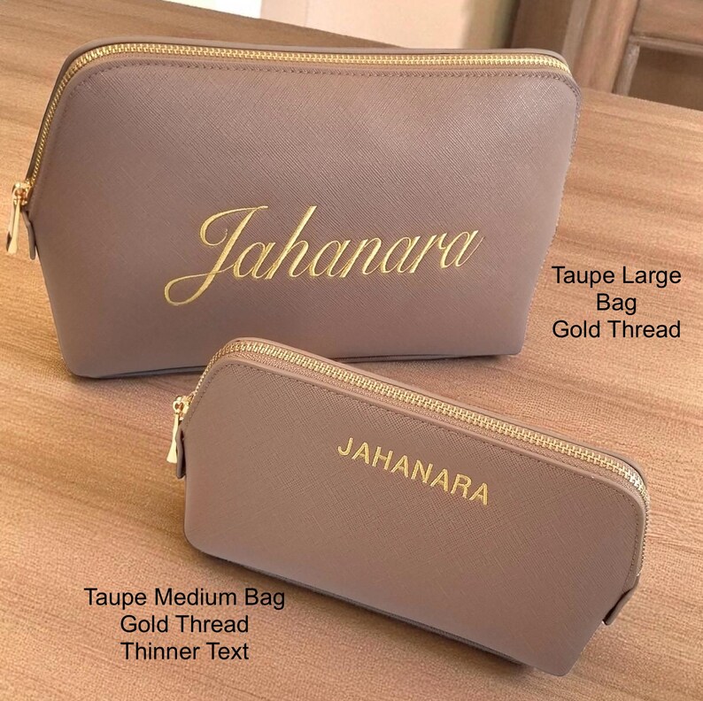 May include: Two taupe cosmetic bags with gold zippers and the name "Jahanara" embroidered in gold script. The larger bag is above the smaller bag. The text "Taupe Large Bag Gold Thread" and "Taupe Medium Bag Gold Thread Thinner Text" are also visible.