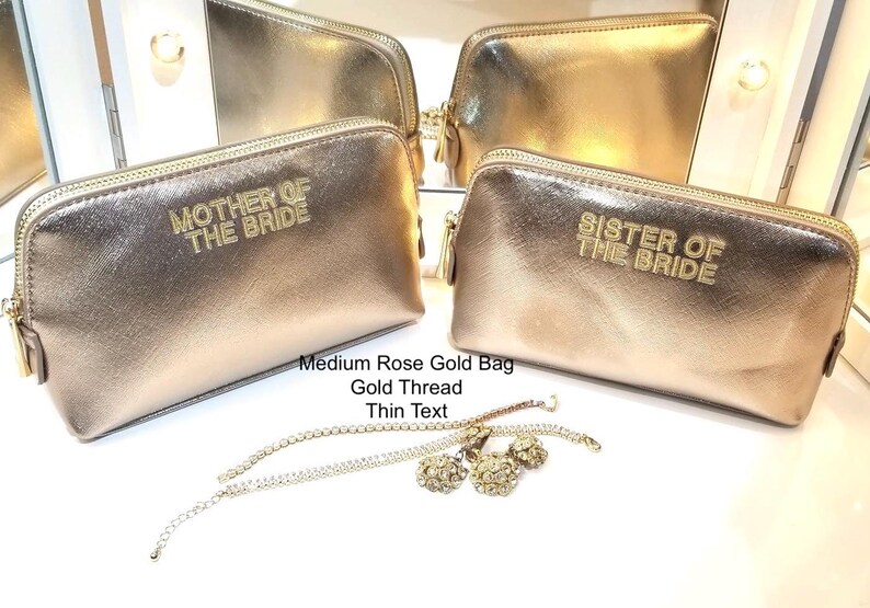 May include: Rose gold cosmetic bags with gold thread text that reads "MOTHER OF THE BRIDE" and "SISTER OF THE BRIDE". The bags have a zipper closure and are displayed with gold jewelry.