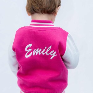 May include: A pink and white baseball jacket with white embroidered lettering that says "Emily" on the back.