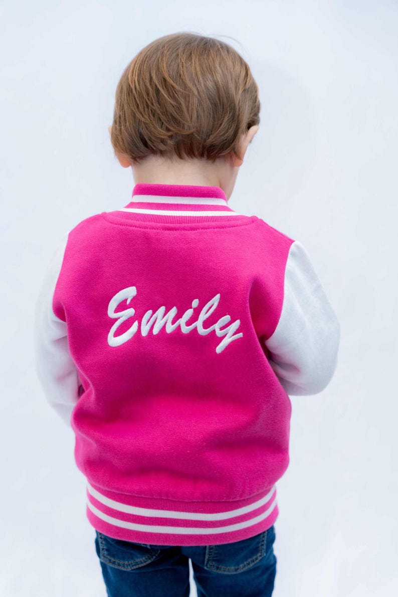 May include: A pink and white baseball jacket with white embroidered lettering that says "Emily" on the back.