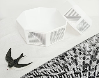 May include: White octagonal storage box with a geometric pattern lid. The box is made of ceramic and has a sleek, modern design.