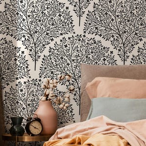 May include: A bedroom scene featuring a bed with peach and gold bedding, a black pillow, and a patterned wallpaper with black tree silhouettes. A small table holds a vase, clock, and decorative items.