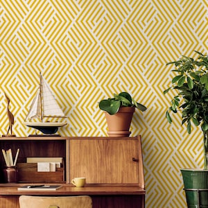 May include: A room scene featuring a wooden desk, chair, and decorative items against a yellow and white geometric patterned wallpaper. The desk holds a small sailboat model, a potted plant, and a cup. Two wooden oars lean against the wall.