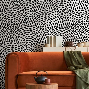 May include: An orange velvet sofa with a wooden side table and a black teapot. A green blanket is draped over the sofa. The background features a black and white patterned wallpaper, creating a stylish living room setting.