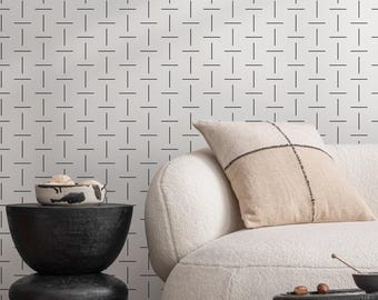 May include: A modern living room scene featuring a white boucle sofa with a beige pillow and a black side table. A black decorative bowl sits on a stacked black side table. The wall has a geometric pattern.