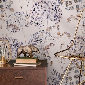 May include: A gold wireframe lamp and a geometric bear sculpture sit on a dark wood nightstand. The background features a floral wallpaper with purple and beige botanical designs. A gold metal chair is on the right.