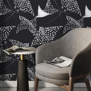 May include: Black and white wallpaper featuring a repeating pattern of spotted eagle rays. The rays have white bellies and are set against a dark background. A gray armchair and a small side table with a marble top are in the foreground.