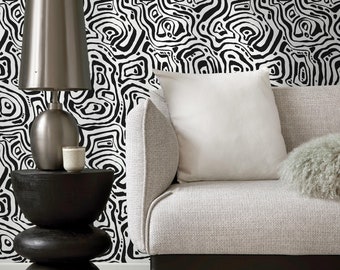 Puede incluir: Un sofá blanco con una pared estampada en blanco y negro detrás. Una lámpara plateada con una pantalla blanca se encuentra sobre una mesa auxiliar negra.