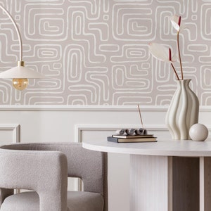 Puede incluir: Una mesa redonda blanca con una silla blanca y un jarrón blanco con flores rojas. La mesa tiene una pila de libros y un pequeño porta incienso. La pared detrás de la mesa tiene un papel tapiz beige con un patrón geométrico blanco.