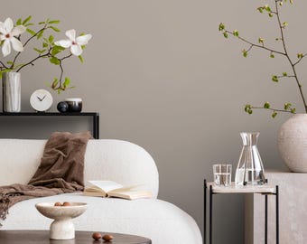 May include: A modern living room scene with a white curved sofa, a dark wood coffee table, and a small side table. Decorative items include a vase with white flowers, a clock, and a bowl with nuts. A brown throw blanket and an open book are on the sofa.