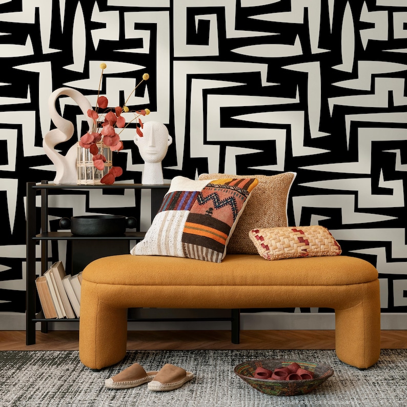 May include: A mustard yellow bench with a black metal frame and two pillows. The bench is in front of a wall with a black and white geometric pattern wallpaper.
