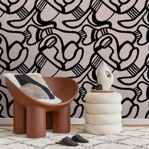 May include: A modern interior scene featuring a brown chair with a patterned pillow, a white side table with a vase, and black slippers. The background has a black and pink abstract design. The rug is white with a black geometric pattern.