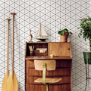 May include: A mid-century modern desk with a wooden chair, decorative items, and a potted plant. The desk has drawers and a small cabinet. Two wooden oars lean against a wall with a black and white geometric pattern.