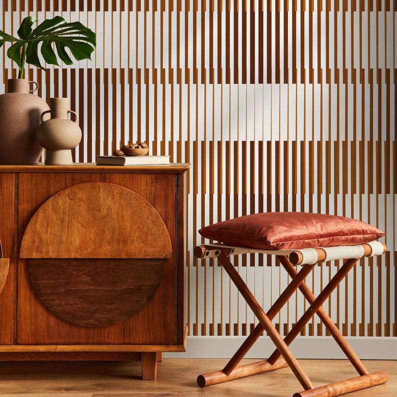 Op de afbeelding: Een houten kast met een halfronde vorm op de voordeur. Een kleine kruk met een rood kussen staat voor de kast. De muur achter de kast is bedekt met een bruin-wit gestreept behang.