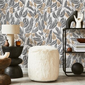 May include: A white faux fur ottoman with a black and beige floral wallpaper background. The ottoman is sitting in front of a black metal shelf with a bowl and books on it.