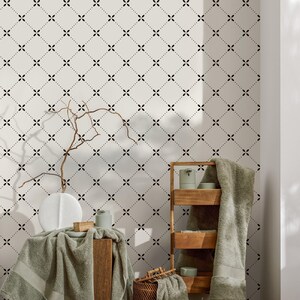 May include: A bathroom scene featuring a cream-colored wall with a black floral pattern. A wooden shelf holds towels and toiletries. A vase and a wooden block are on a wooden stand, draped with a green towel. A wicker basket is on the floor.