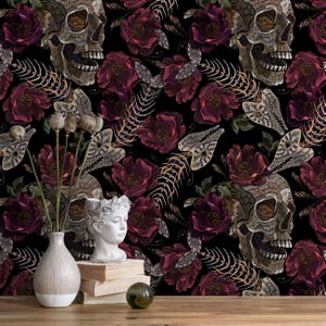 May include: A dark, gothic-themed wallpaper featuring embroidered skulls, burgundy roses, and moth illustrations against a black background. The design includes a vase, a bust, books, and a decorative glass ball on a wooden surface.