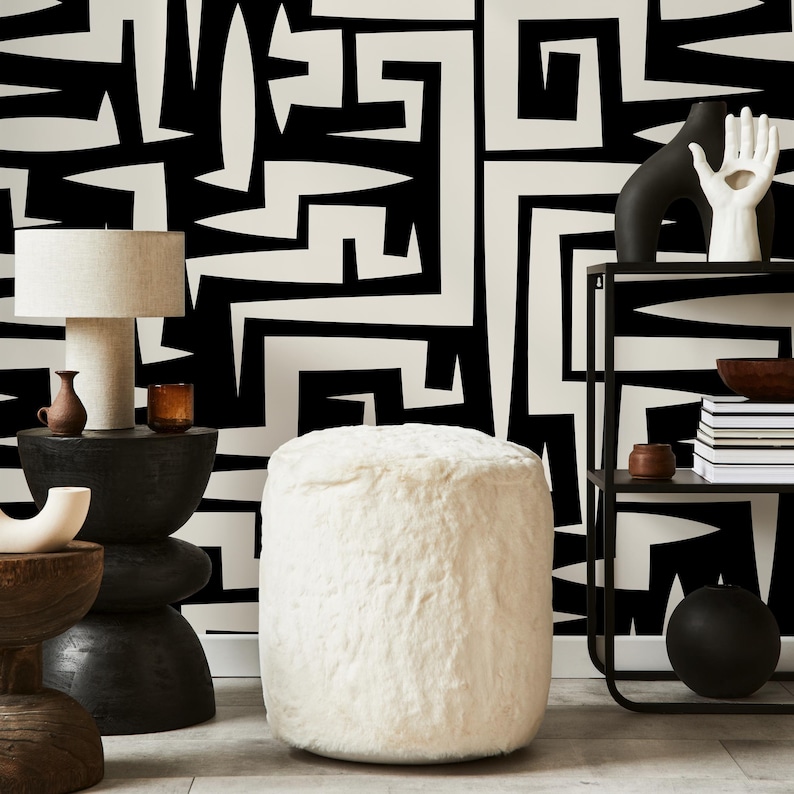 May include: White faux fur ottoman with a black and white geometric patterned wall behind it. The ottoman is round and sits on a wooden floor.