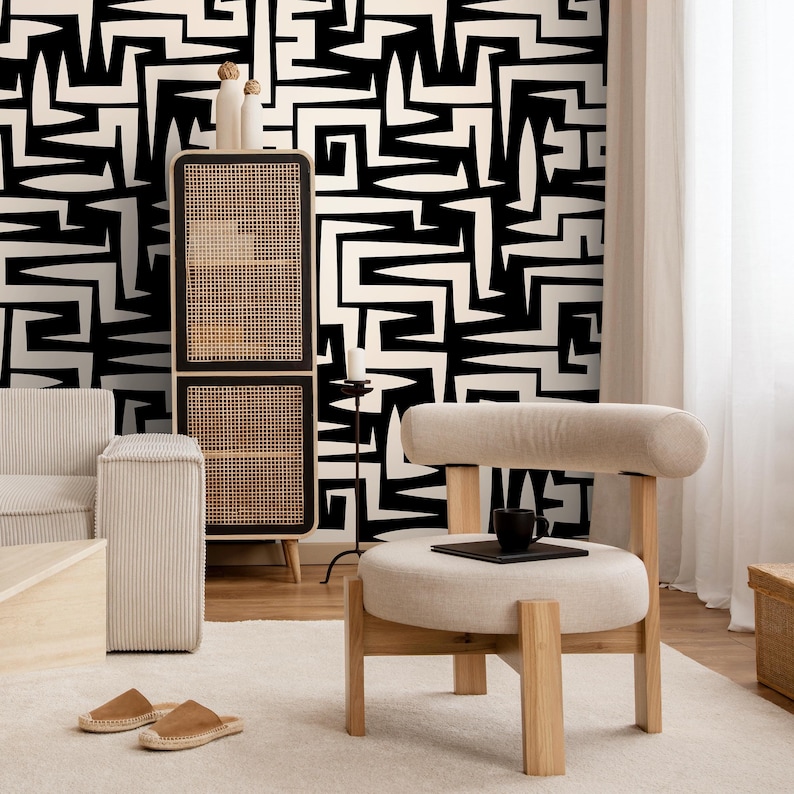 May include: A black and white geometric patterned wallpaper with a black metal stand and a white upholstered chair with a round seat and wooden legs. The chair is in front of a black and white patterned wallpaper.