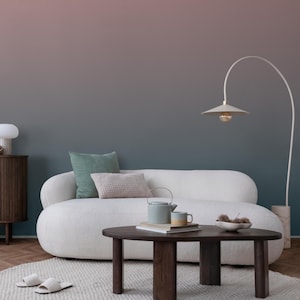 May include: A modern living room with a white sofa, green and beige pillows, and a dark wood coffee table. A light blue teapot and cup sit on the table, along with books and a bowl of decorative items. A tall, arched lamp and a wooden cabinet are also visible.