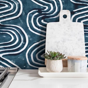 May include: A white marble chopping board with a hole, a small succulent in a white pot, and a decorative jar with a wooden lid sit on a white tray. The background features a blue and white abstract pattern.