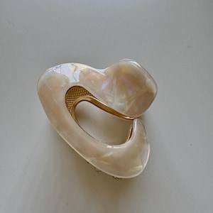 May include: A white and gold heart-shaped hair clip with a pearlescent finish.