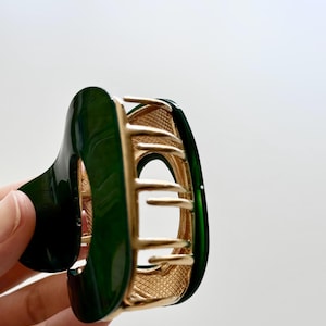 May include: A green and gold hair claw with a decorative design. The claw is made of plastic and metal.