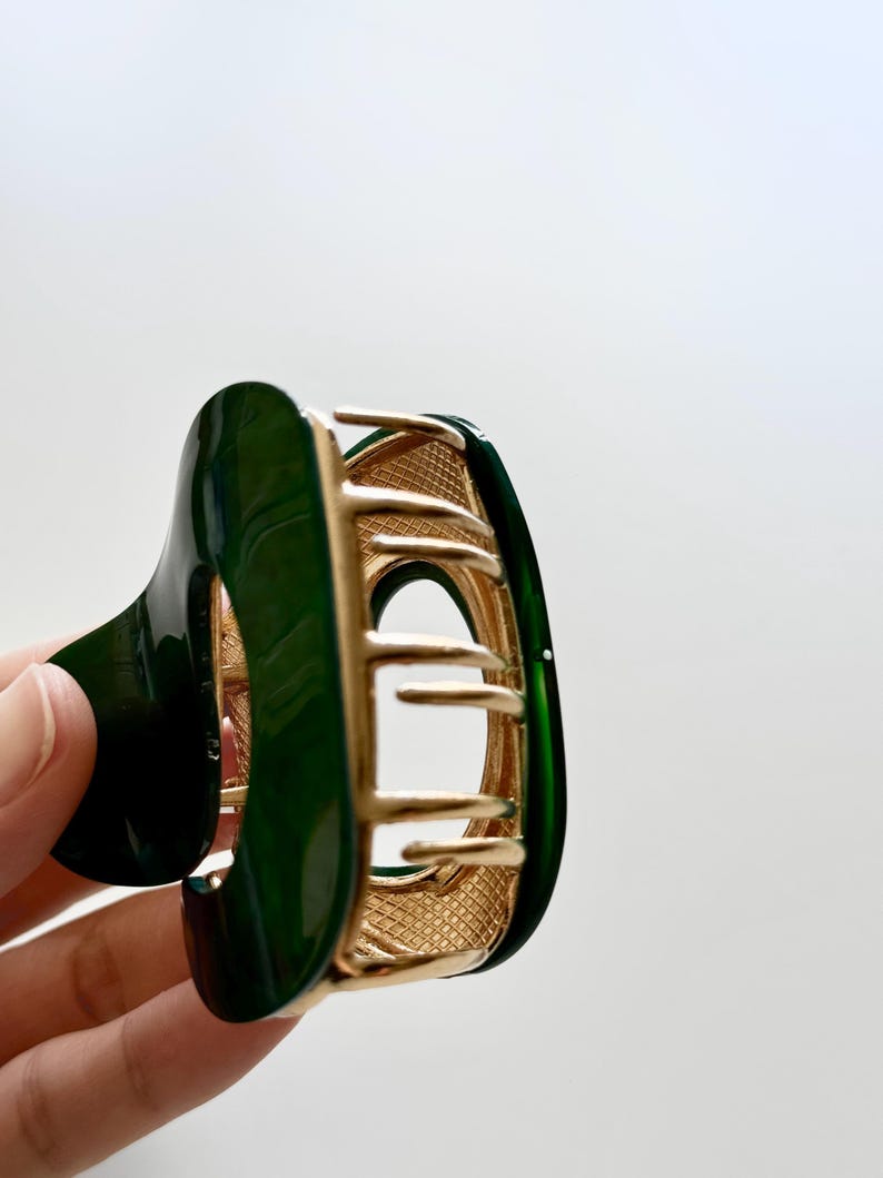 May include: A green and gold hair claw with a decorative design. The claw is made of plastic and metal.