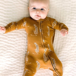 Puede incluir: Un bebé con un pijama de manga larga con cremallera de color marrón y amarillo con estampado de guepardo.