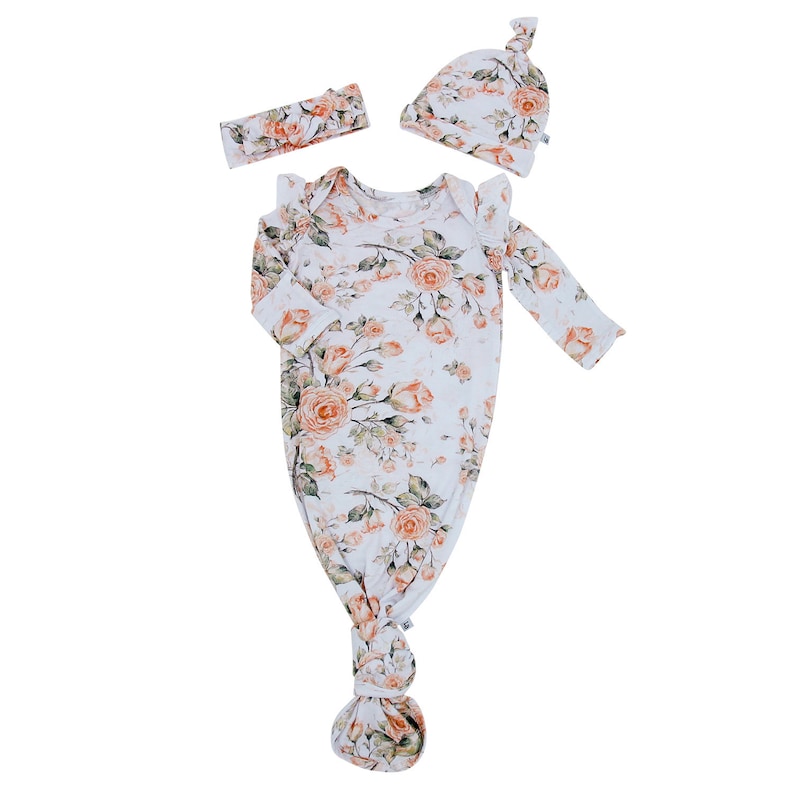 May include: A baby gown, hat and headband set in a floral print with orange roses on a white background.
