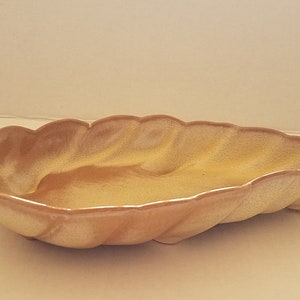 May include: A ceramic serving dish shaped like a leaf, glazed in a light brown and yellow colour.